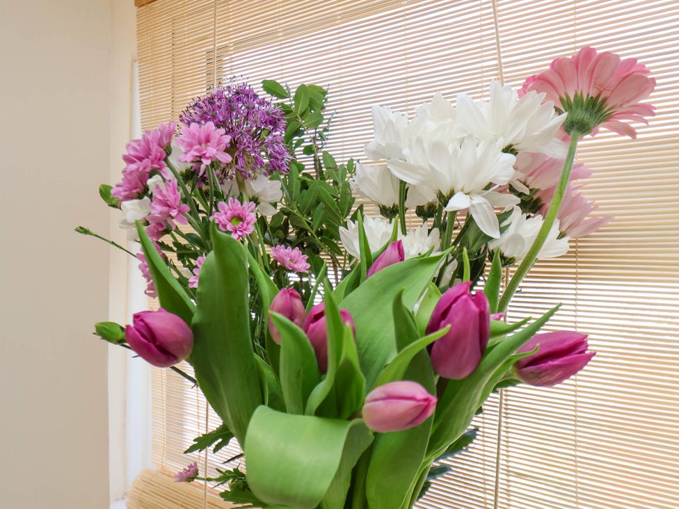 A bouquet of pink and white flowers with green leaves in front of window blinds at Flat 1 in Scarborough