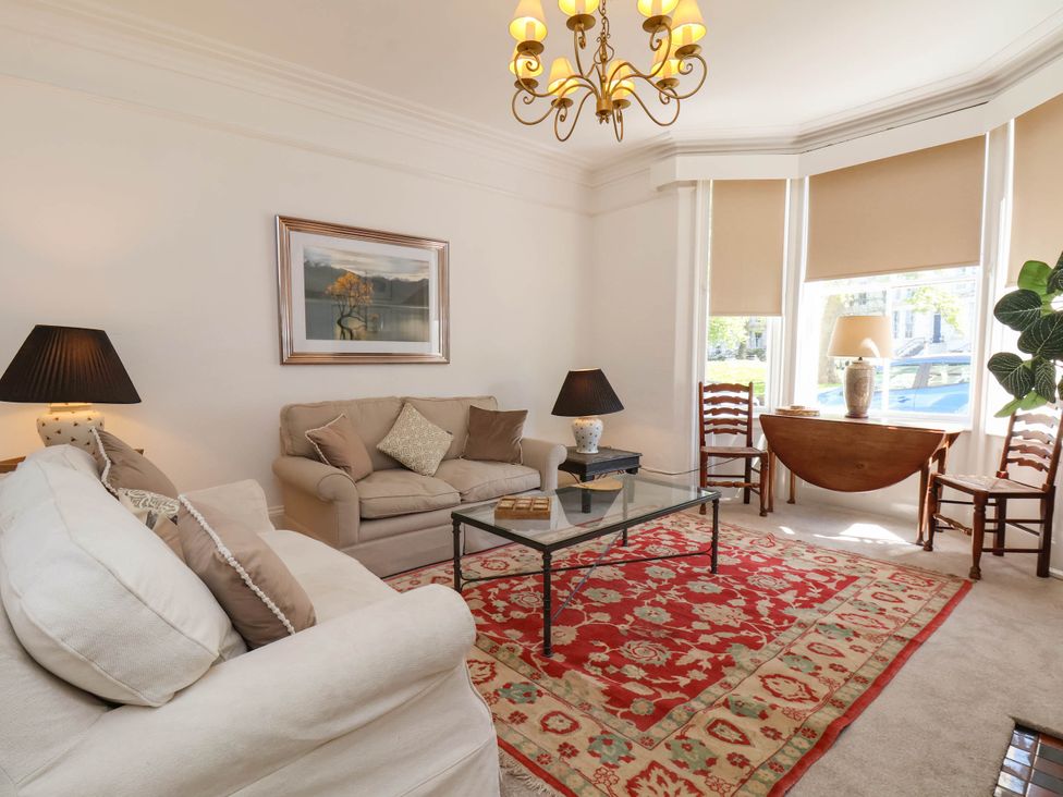 A living room with sofas coffee table red patterned rug and window with shades at Flat 1 in Scarborough