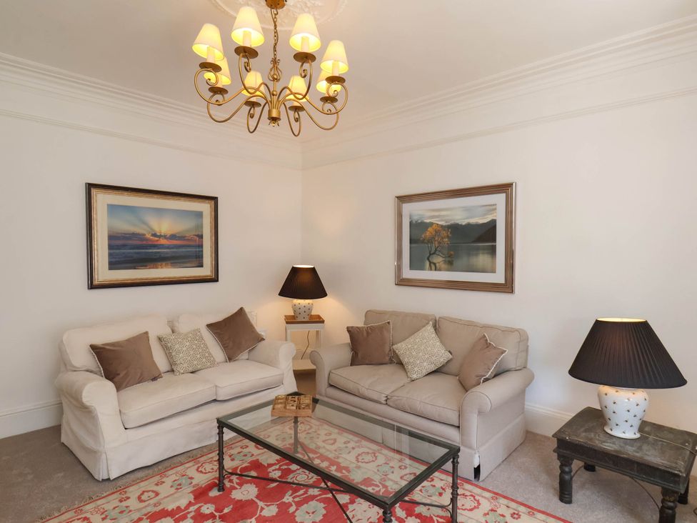A living room with two sofas a glass coffee table two table lamps and framed pictures on walls at Flat 1 in Scarborough