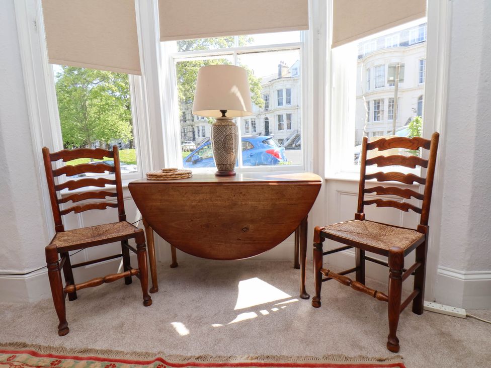 A small wooden table with a lamp and coasters between two wooden chairs in front of bay windows at Flat 1 in Scarborough