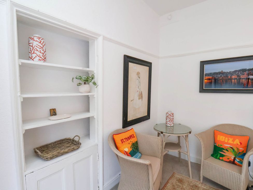 A small seating area with two wicker chairs and a round glass table between them with cushions and framed pictures on the walls at Flat 1 in Scarborough