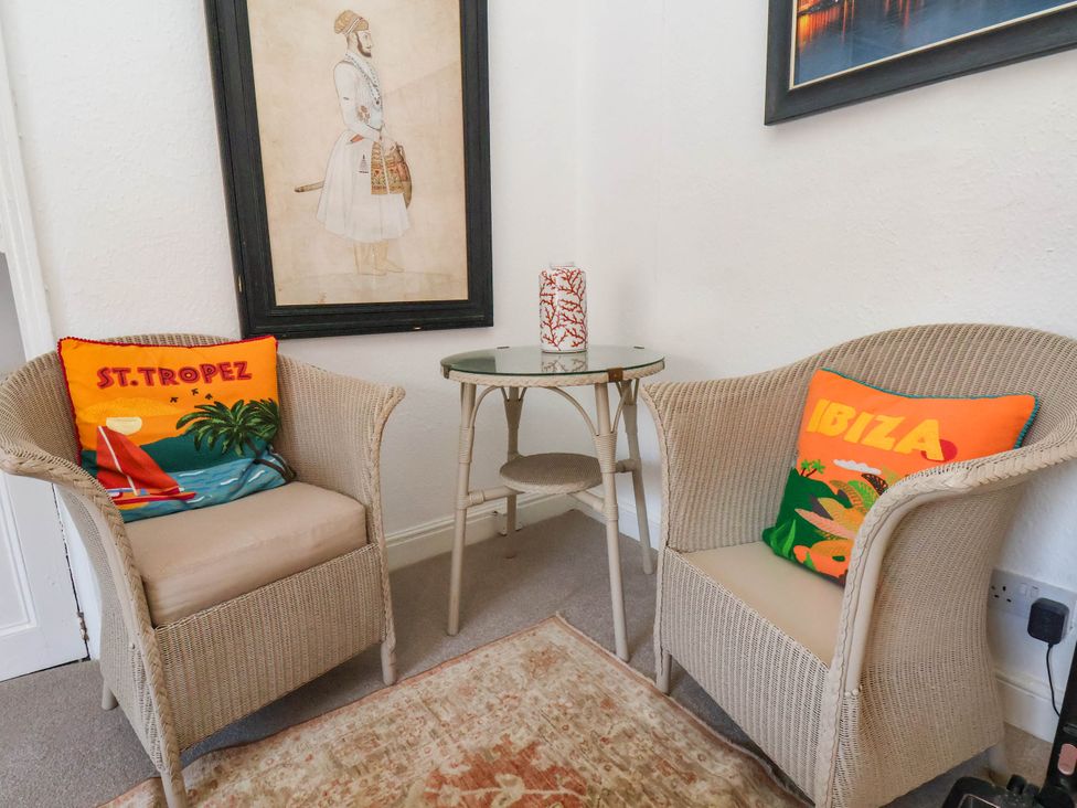 A corner with two wicker armchairs with colorful cushions and a small glass top table with a decorative item at Flat 1 in Scarborough