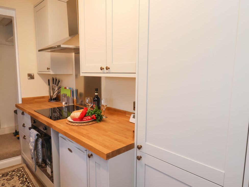 A kitchen with white cabinets wooden countertop a stove a bread loaf red peppers a bottle and two wine glasses at Flat 1 in Scarborough