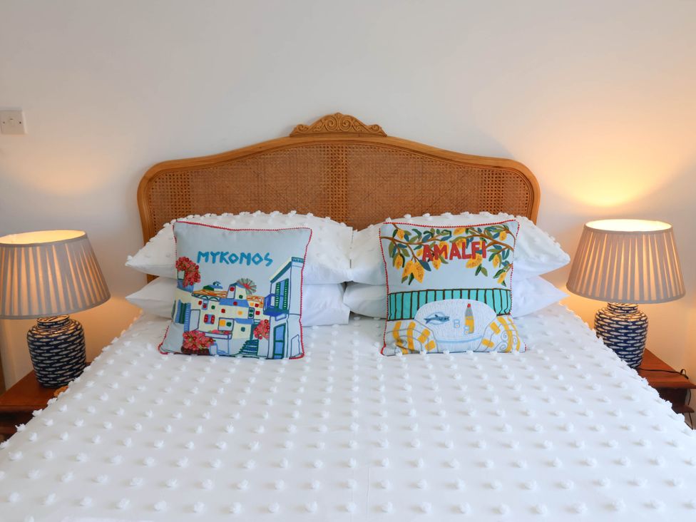 A bed with a woven headboard and two decorative pillows labeled Mykonos and Amalfi with two lamps on bedside tables at Flat 1 in Scarborough