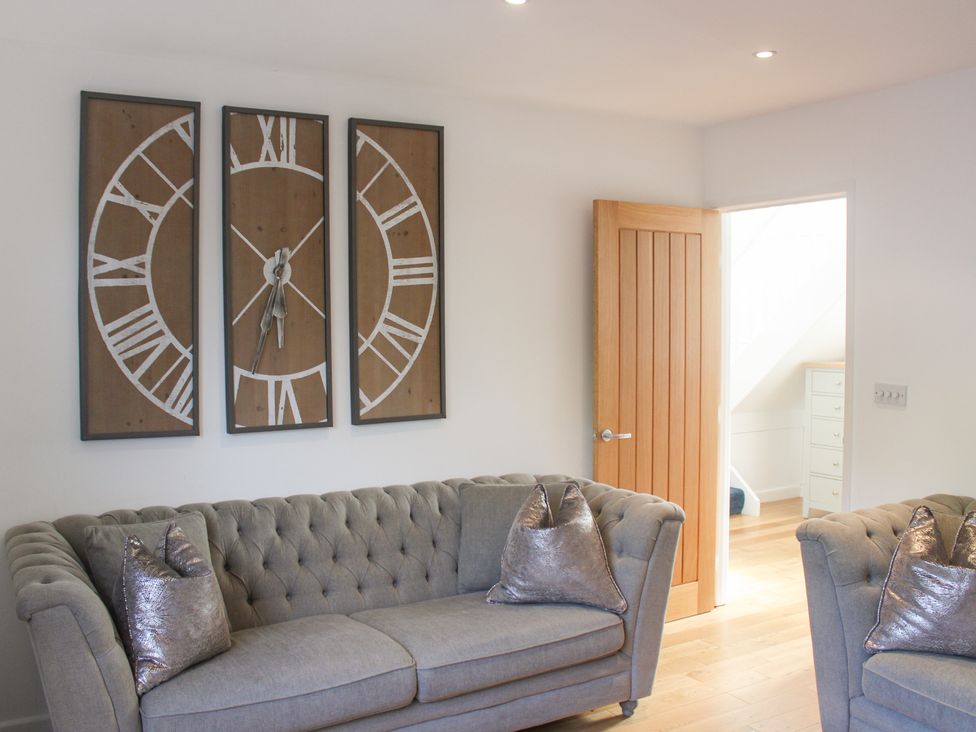 A living room with a clock and two grey sofas at Old Police House in Salcombe