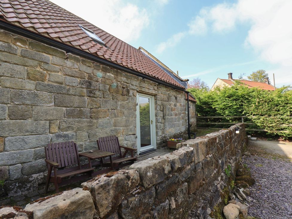 An outdoor area with stone wall and wooden chairs at Horseshoe Cottage in Ingleby Greenhow near Great Ayton