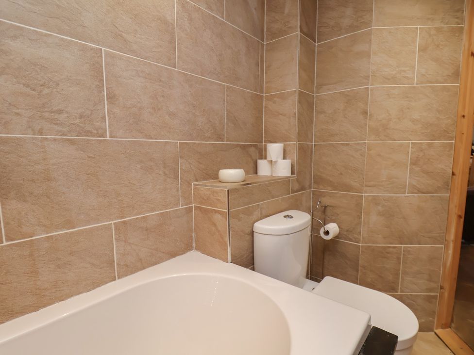 A bathroom with a bathtub, toilet, and storage at Horseshoe Cottage Ingleby Greenhow near Great Ayton