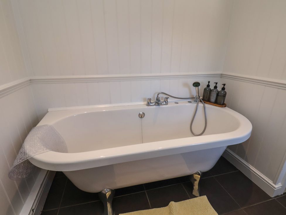 A bathroom with a bathtub and soap dispensers at Seashell Cottage