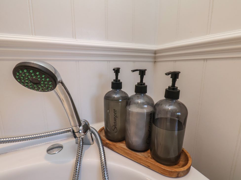 A showerhead and three bottles on a tray in a bathroom at Seashell Cottage