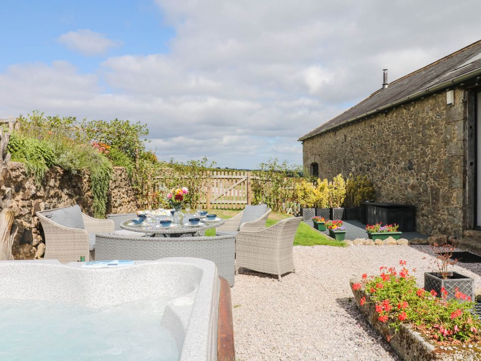 An outdoor seating area with a hot tub and flowers at Halshanger Barn in Newton Abbot