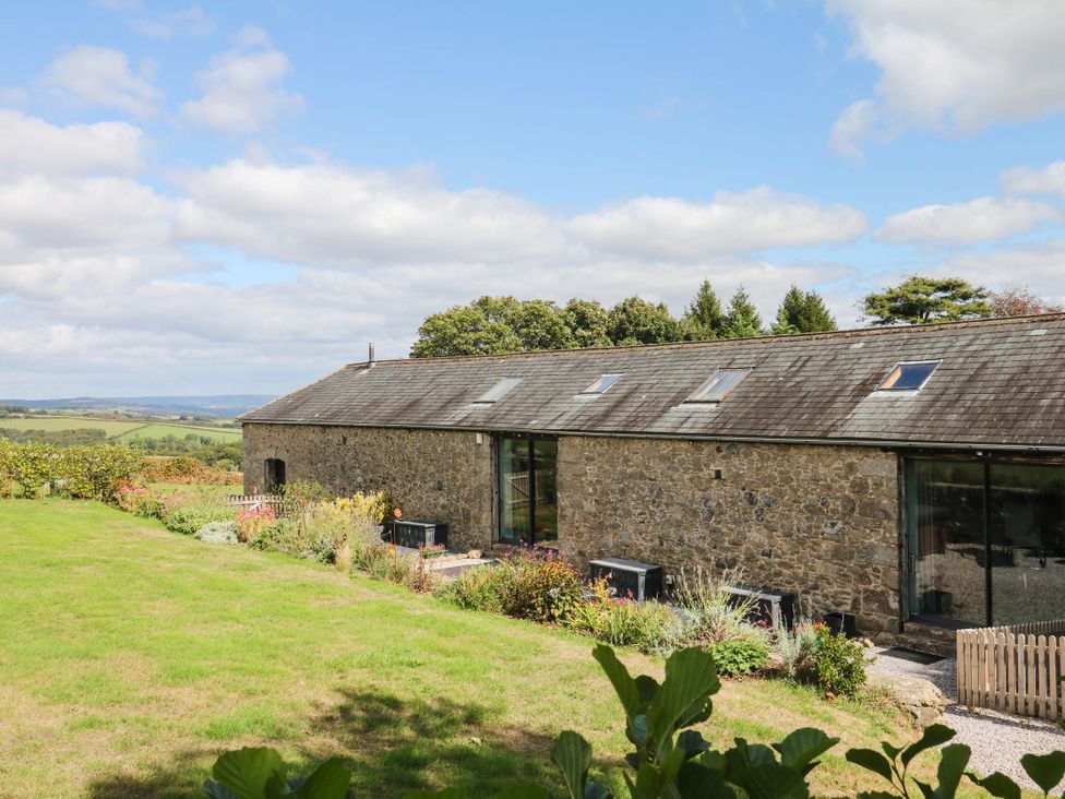 An outdoor view of a stone barn with trees and grass at Halshanger Barn in Newton Abbot
