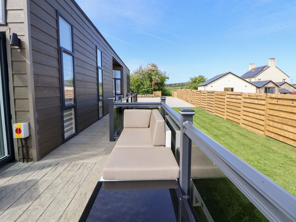 A deck with a couch overlooking grass and a fence at The Lodge @ Racecourse House Babell near Holywell