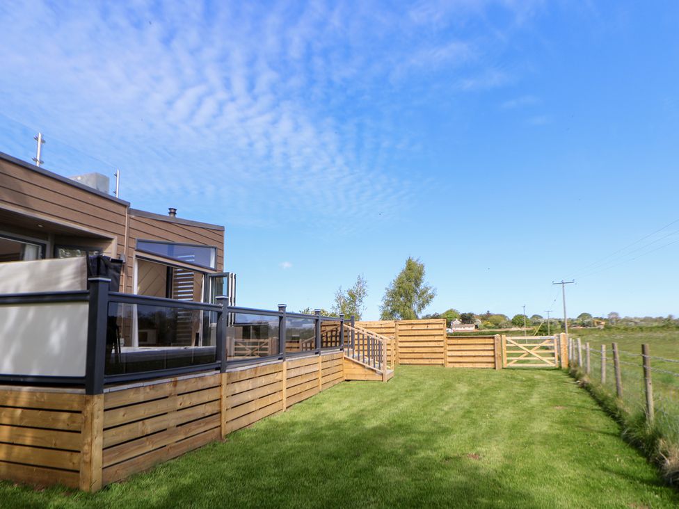 A garden with wooden decking and a fence at The Lodge @ Racecourse House in Babell near Holywell