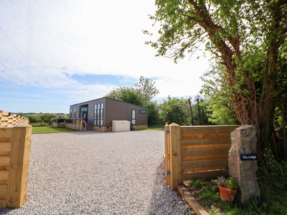 A lodge with a gravel driveway and wooden fence at The Lodge @ Racecourse House in Babell near Holywell