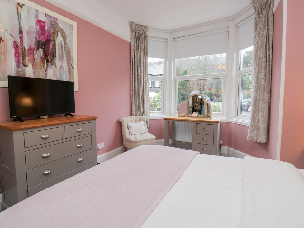 A bedroom with a television, dresser, vanity table, and armchair at The Wonky Nest in Bowness-On-Windermere
