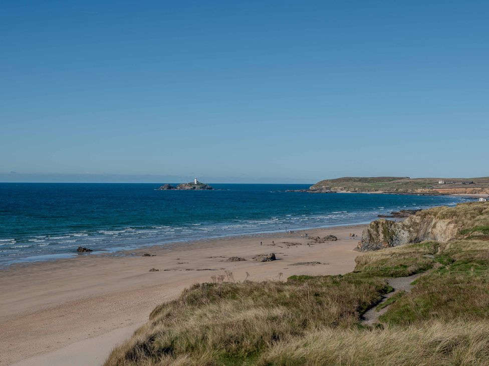 A beach with a distant lighthouse and rock formations at Chalet 3 Wipeout in Hayle