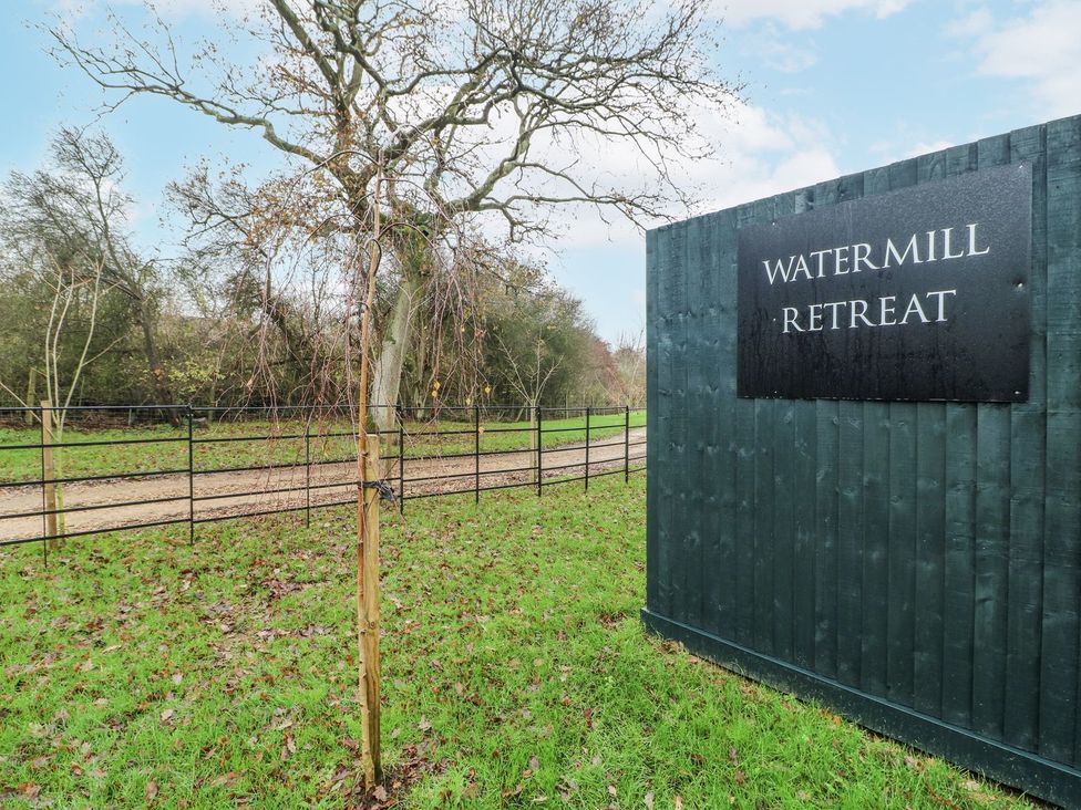 A sign at the entrance of Watermill Retreat with a tree and gravel pathway at Badger's Burrow Edith Weston
