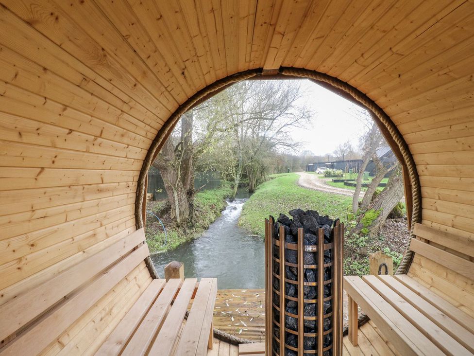 A wooden structure with benches and a stove overlooking a stream at Badger's Burrow in Edith Weston