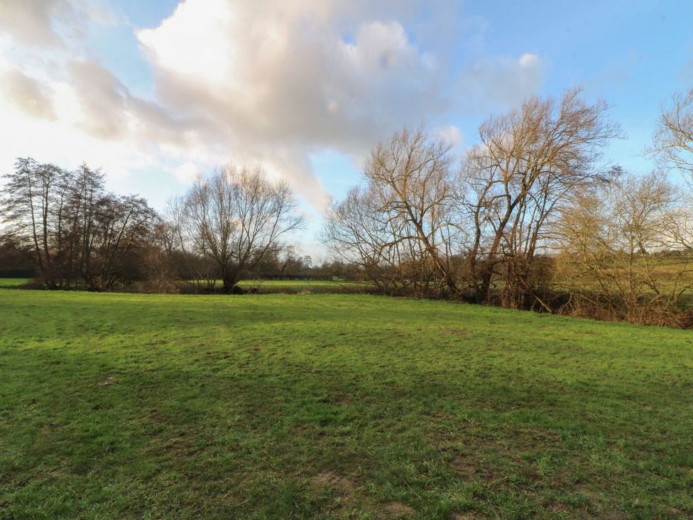 A grassy area with trees and a cloudy sky at Badger's Burrow in Edith Weston