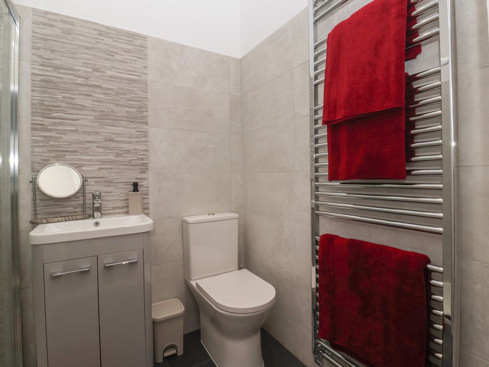A bathroom featuring a sink, toilet, mirror, and red towels at Virginia Cottage in Skipton