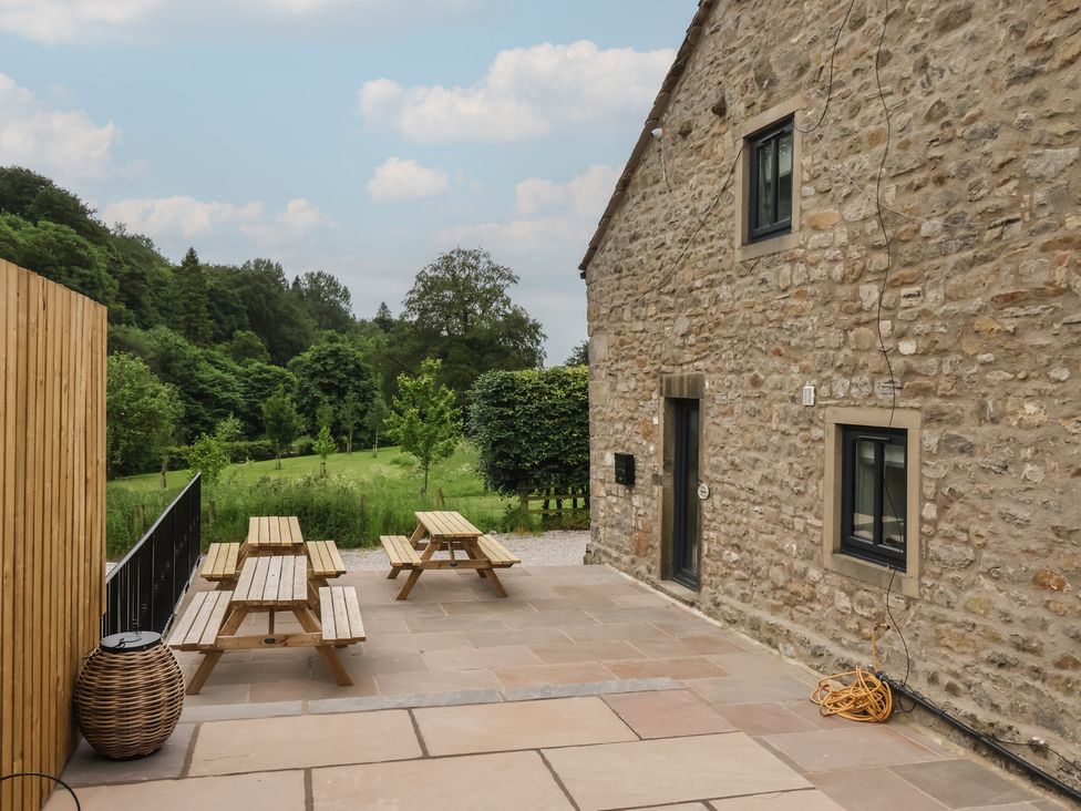 A patio with wooden tables and benches at Virginia Cottage in Skipton