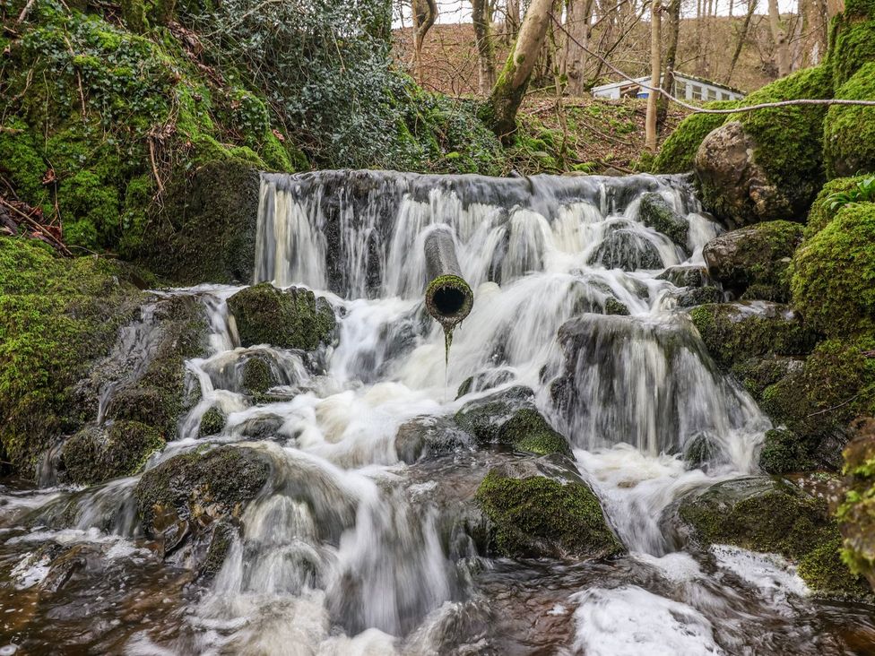 A waterfall flowing over rocks in a wooded area at Virginia Cottage Hetton