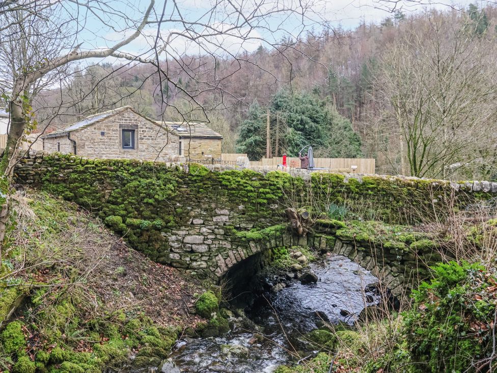 A stone bridge over water with a house and trees at Beckside in Skipton