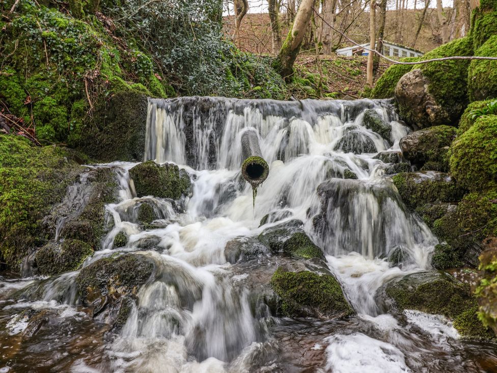 A waterfall with a drain pipe surrounded by rocks and moss at Beckside in Skipton