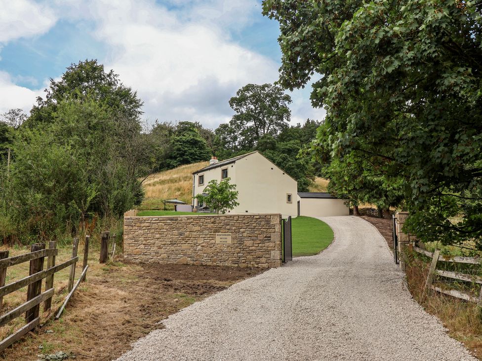 A house with a gravel driveway and stone wall at Wood Cottage in Winterburn