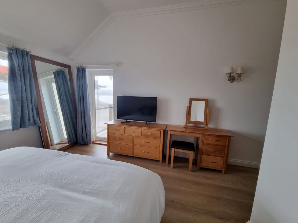 A bedroom with a bed, television, dresser, mirror, and chair at Sea View Beach Apartment Thurlestone