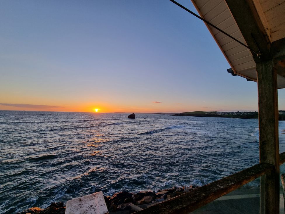 A sunset over the ocean with a rock in the water at Sea View Beach Apartment Thurlestone