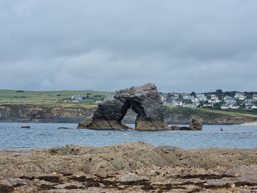 A rock formation in water with houses in the background at Sea View Beach Apartment Thurlestone