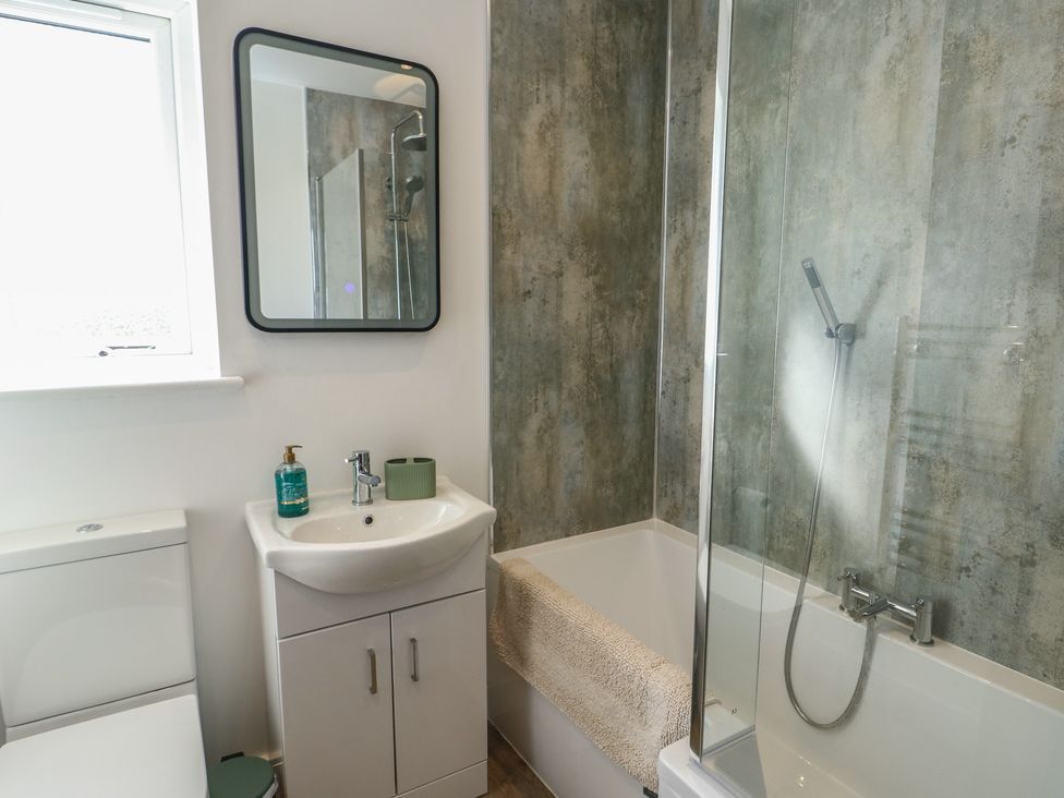 A bathroom featuring a toilet, sink, mirror, and bathtub at 36 Parc Delfryn