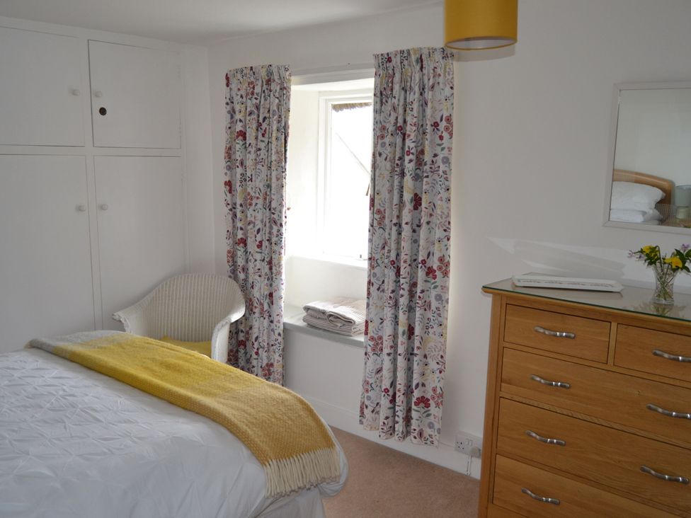 A bedroom with a bed, curtains, and a dressing table at Vine Cottage in East Prawle