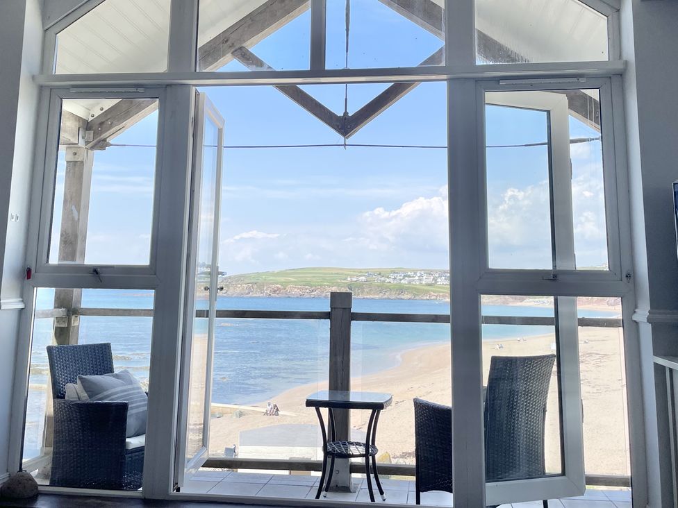 A balcony with two wicker chairs and a small table overlooking a beach and sea at 12 Thurlestone Rock in Thurlestone