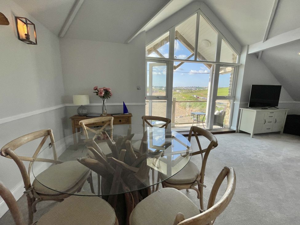 A dining area with a round glass table and six chairs near large windows and a door leading outside at 12 Thurlestone Rock in Thurlestone