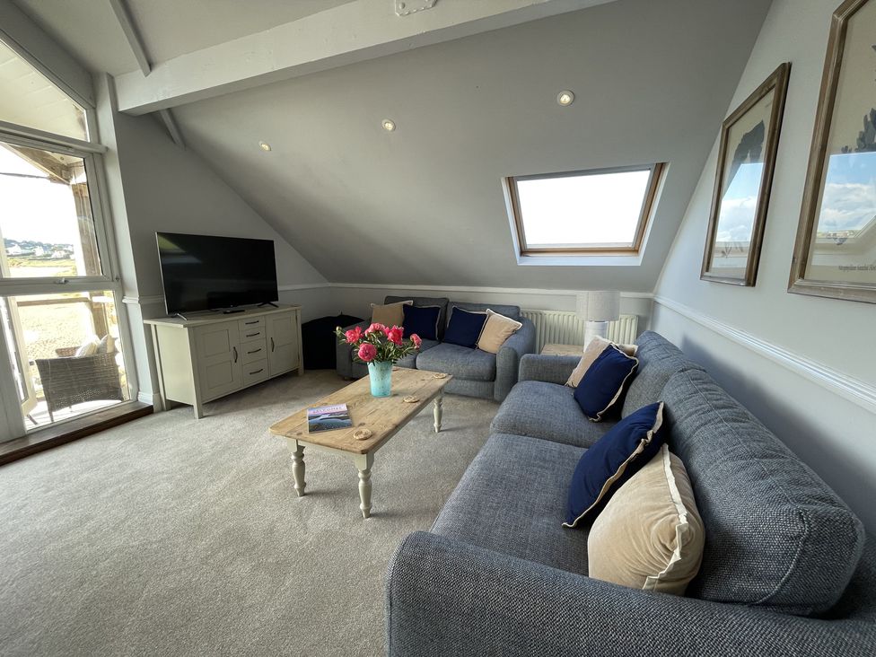 A living room with blue sofas a wooden coffee table with flowers a television and skylight window at 12 Thurlestone Rock in Thurlestone