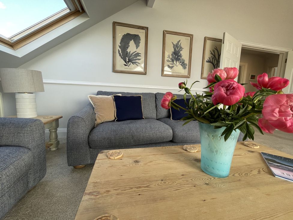 A living room with a gray sofa blue and beige cushions a wooden coffee table with pink flowers in a blue vase and framed artwork on the wall at 12 Thurlestone Rock in Thurlestone