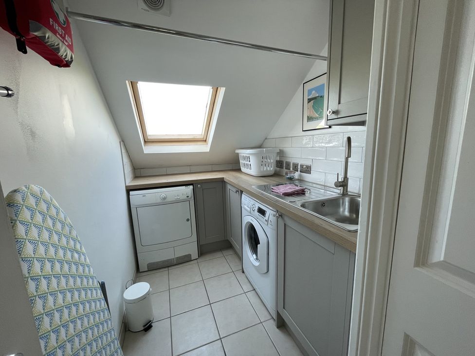 A utility room with a washing machine dryer sink laundry basket and an ironing board at 12 Thurlestone Rock in Thurlestone