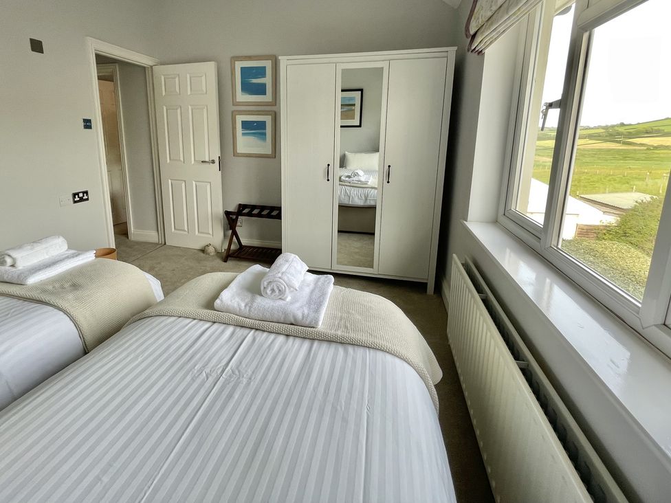 A bedroom with two single beds a white wardrobe with a mirror and a window showing a landscape at 12 Thurlestone Rock in Thurlestone