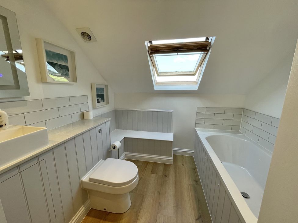 A bathroom with a toilet bathtub skylight and framed pictures on the wall at 12 Thurlestone Rock in Thurlestone