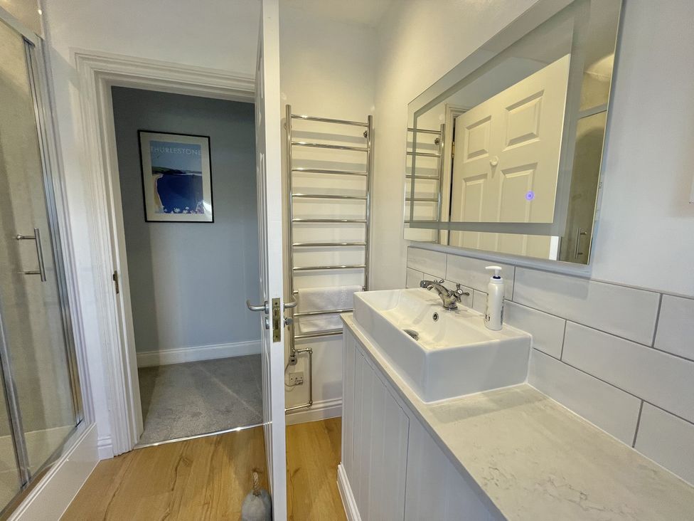 A bathroom with a sink and mirror and a partially open door showing a towel rack and a framed picture at 12 Thurlestone Rock in Thurlestone
