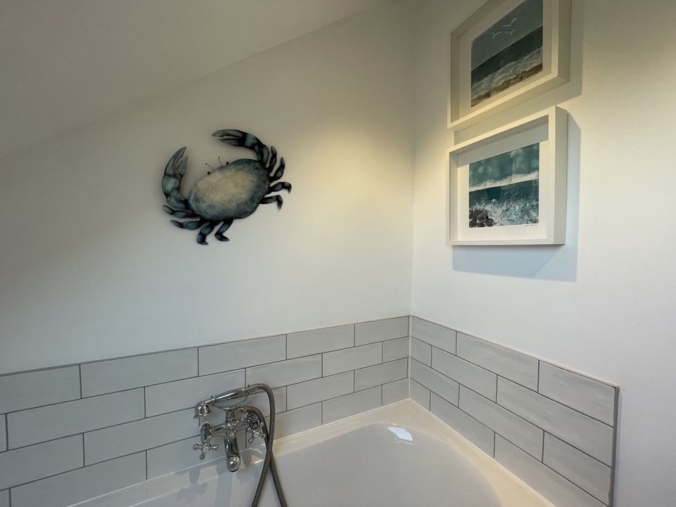 A bathroom corner with a bathtub faucet metal crab wall decoration and two framed ocean pictures at 12 Thurlestone Rock in Thurlestone