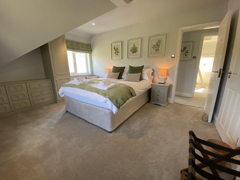 A bedroom with a double bed green pillows bedside tables lamps and built in drawers at 12 Thurlestone Rock in Thurlestone