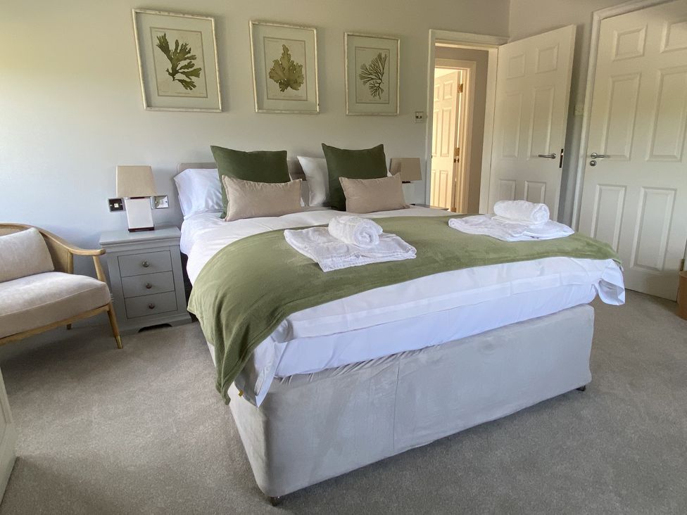 A bedroom with a double bed green throw pillows and towels on the bed armchair bedside table lamps and three framed botanical prints on the wall at 12 Thurlestone Rock in Thurlestone