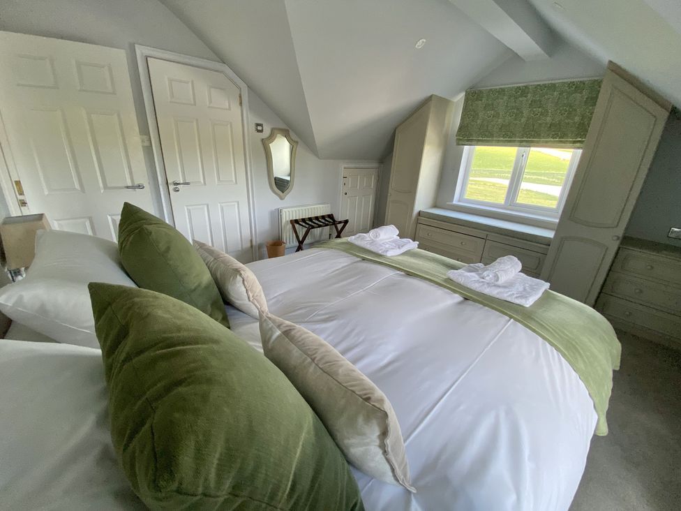 A bedroom with a bed with green and beige pillows and towels on top beside a window with green blinds and built-in storage at 12 Thurlestone Rock in Thurlestone
