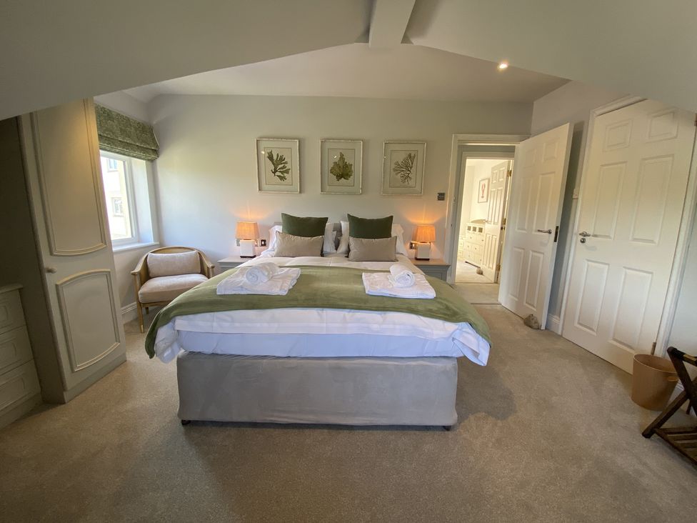 A bedroom with a bed and green blanket two lamps a chair and framed pictures on the wall at 12 Thurlestone Rock in Thurlestone