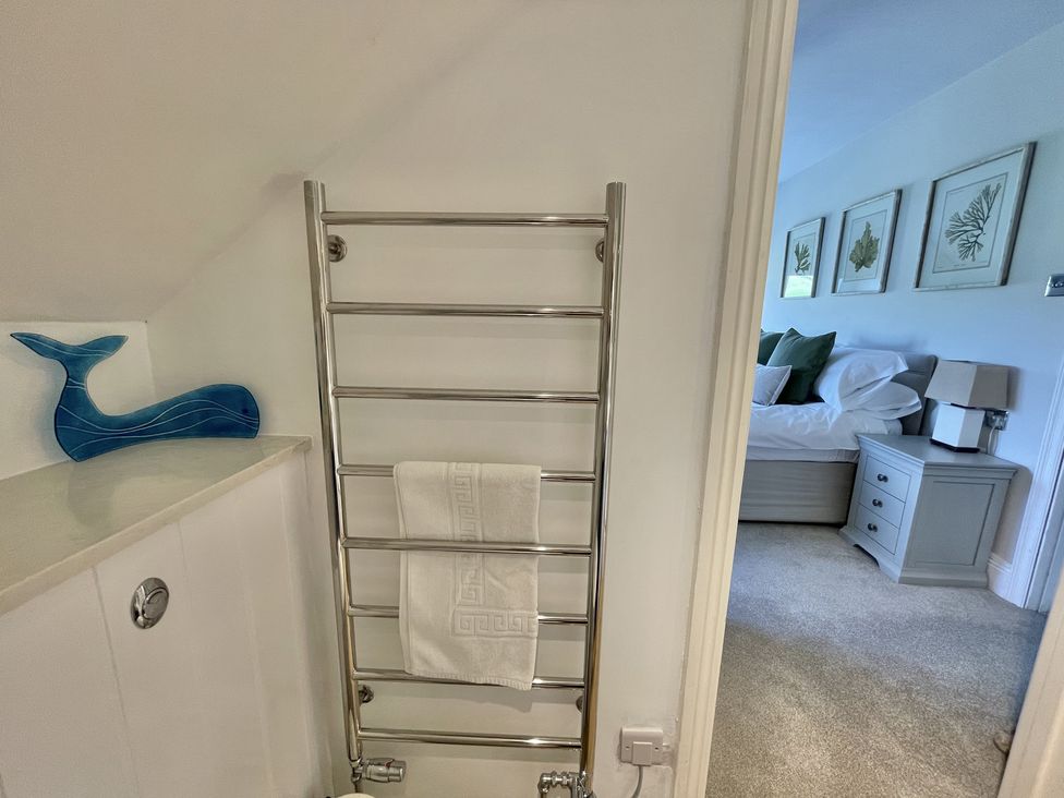 A bathroom with a towel rack and a blue whale decoration next to a doorway showing a bedroom with a bed and framed pictures on the wall at 12 Thurlestone Rock in Thurlestone