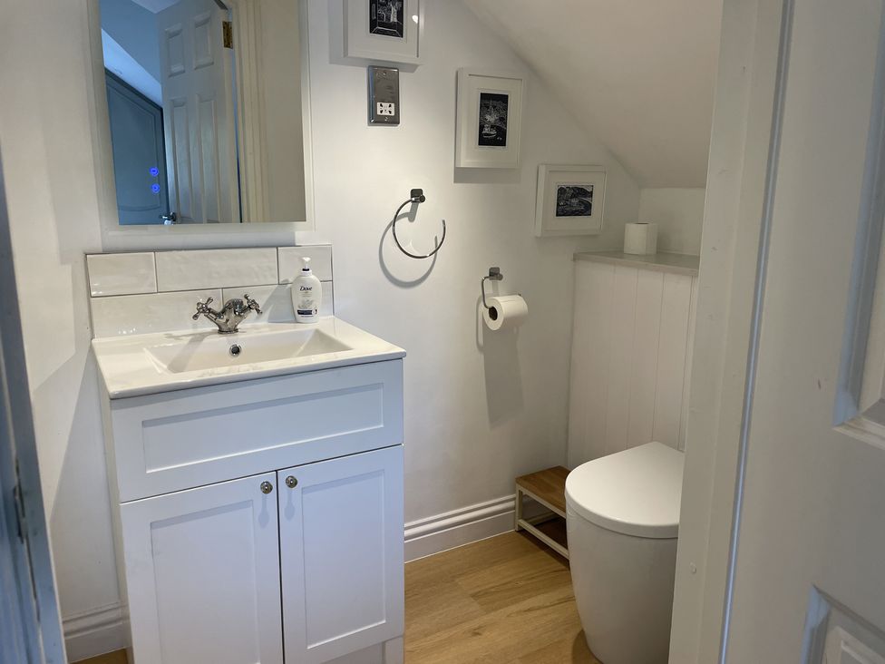 A bathroom with a white sink cabinet a mirror toilet and framed pictures on the wall at 12 Thurlestone Rock in Thurlestone