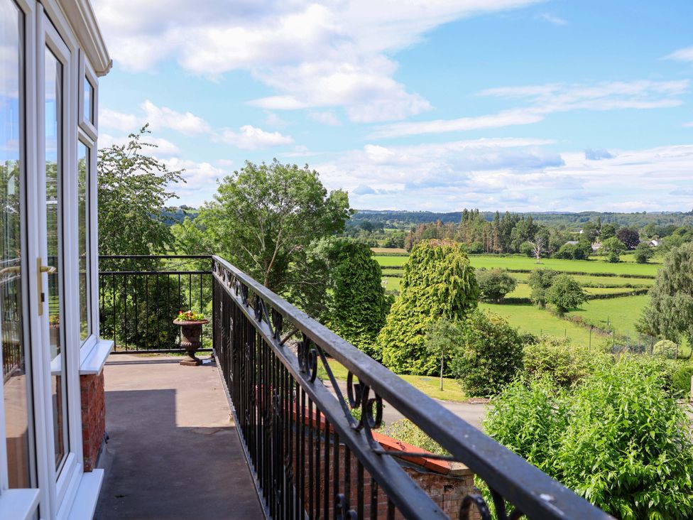 A view from a balcony showing trees and fields at The Old Barn in Pentre Celyn